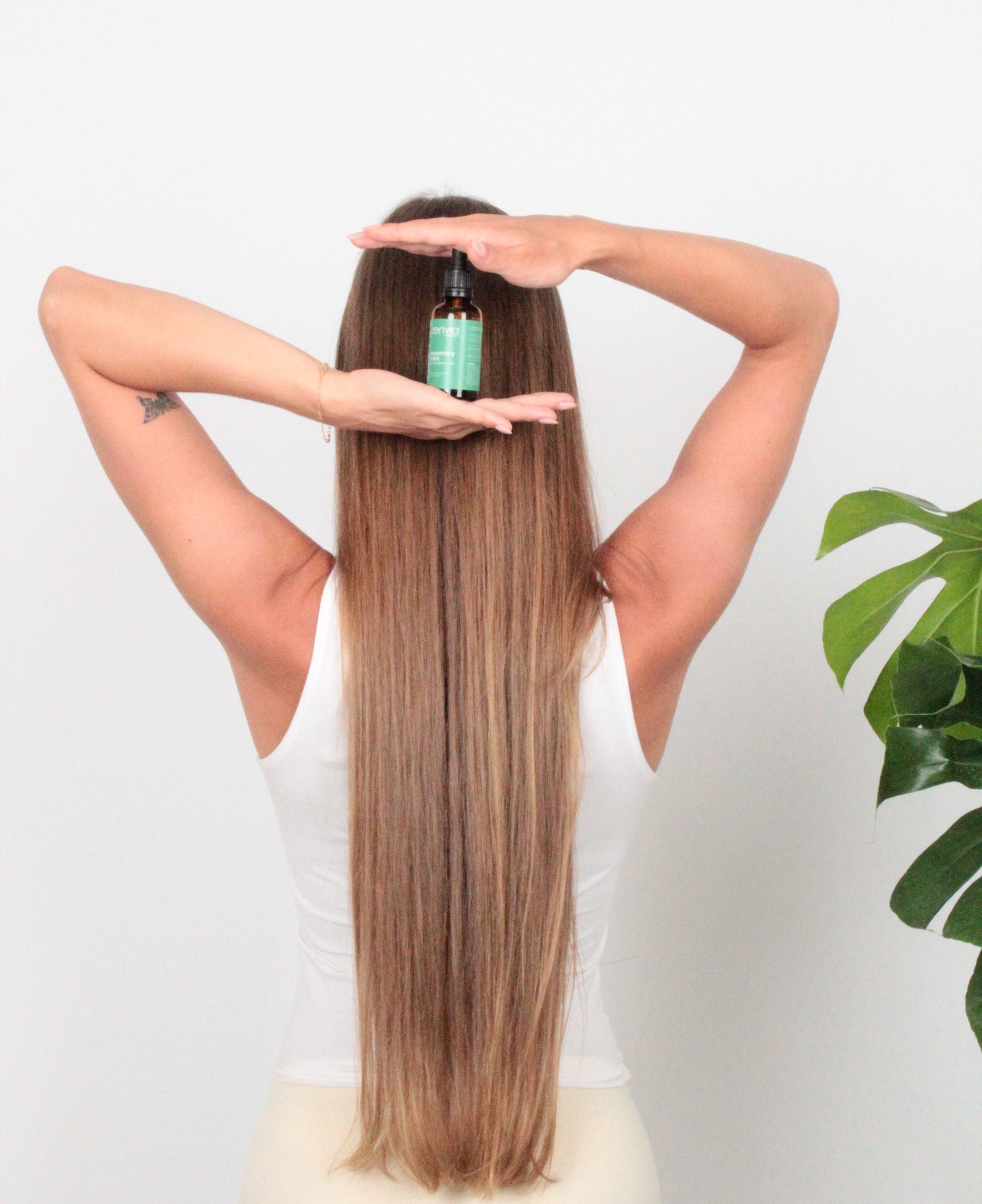 Person holding a bottle of Zenvia Hair Strengthening Oil with long, strong hair against a white background