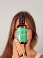 Woman holding a bottle of Zenvia hair strengthening oil against a plain background