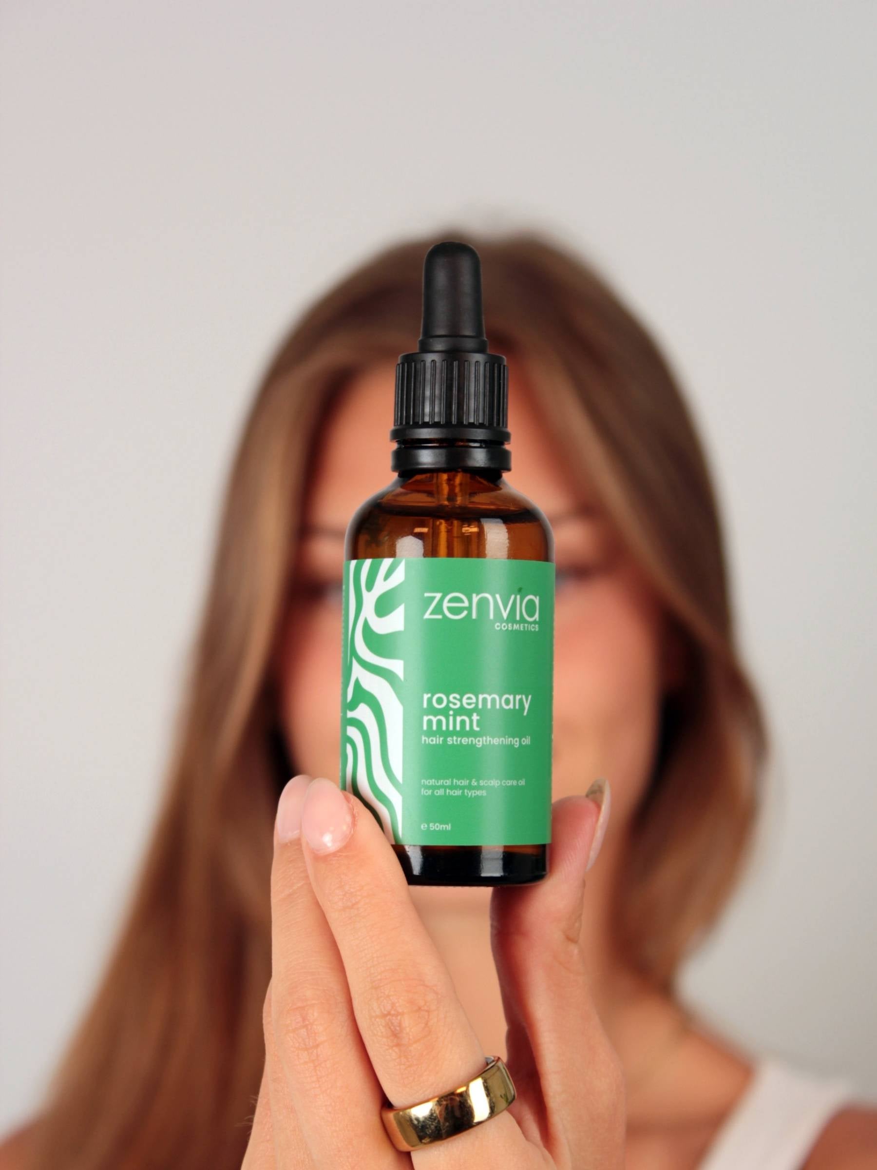 Woman holding a bottle of Zenvia rosemary mint oil against a plain background