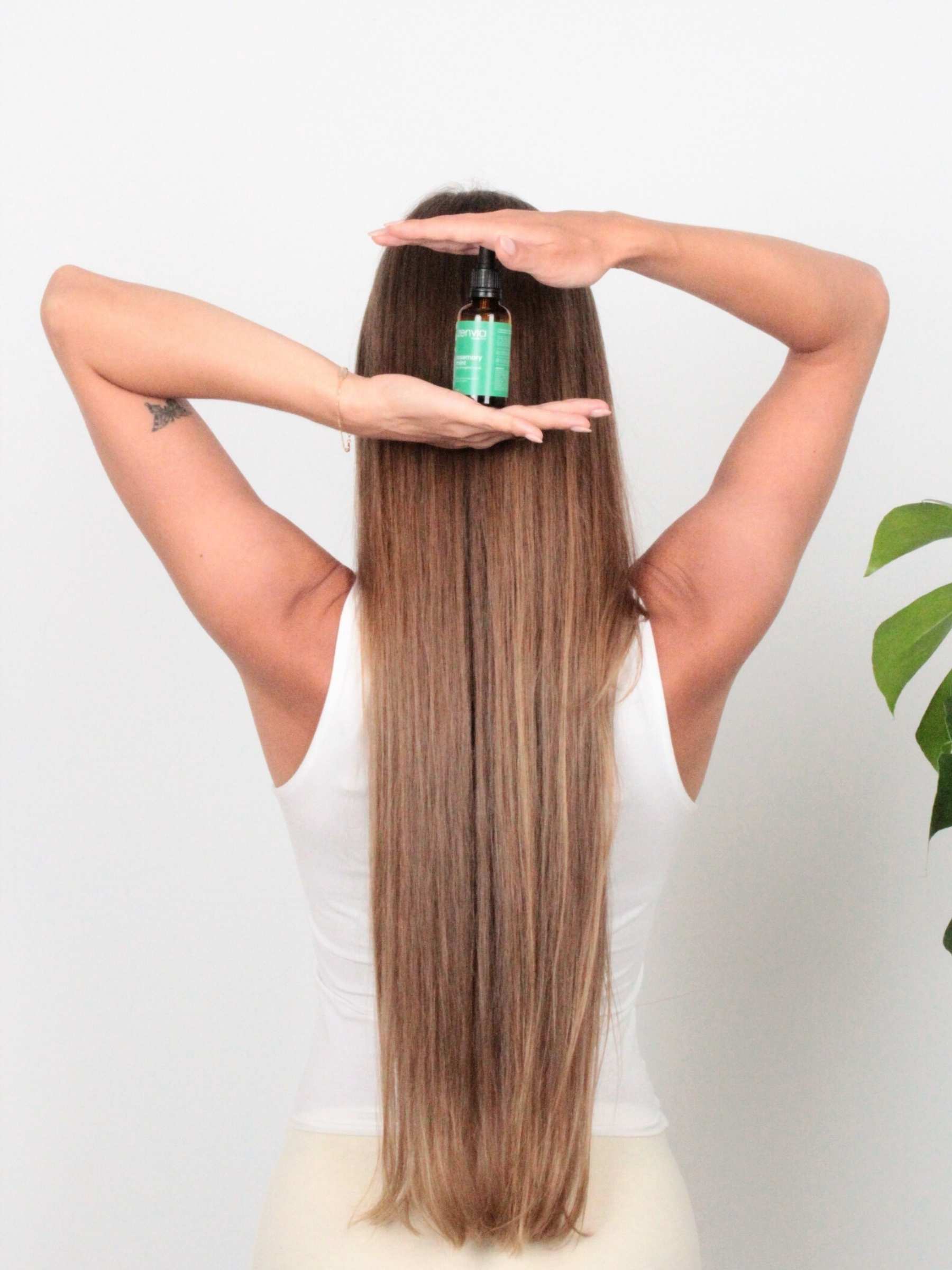Woman with long and strong hair holding a Zenvia scalp oil against a white background