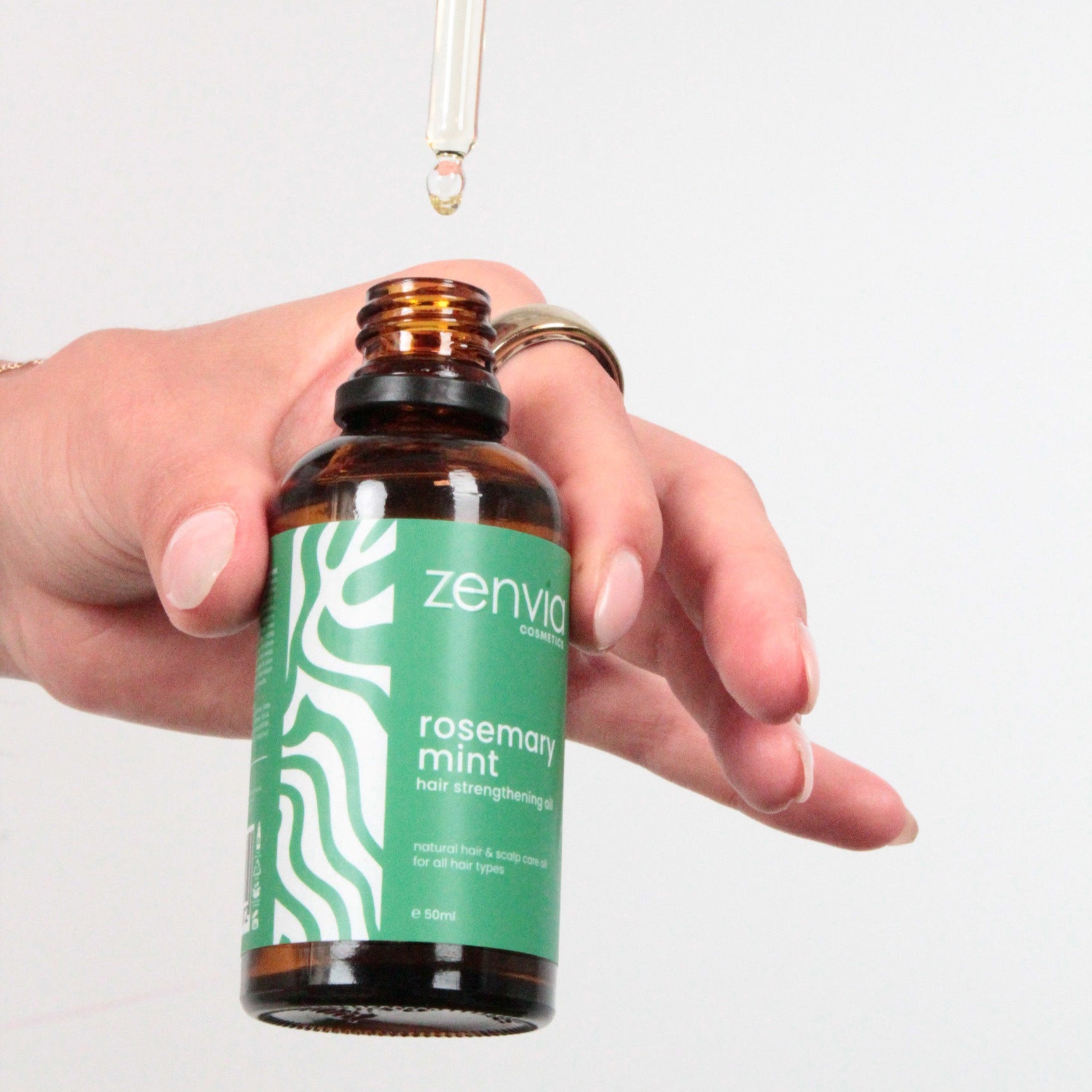 Bottle of Zenvia rosemary mint oil with a dropper held by a hand on a light gray background