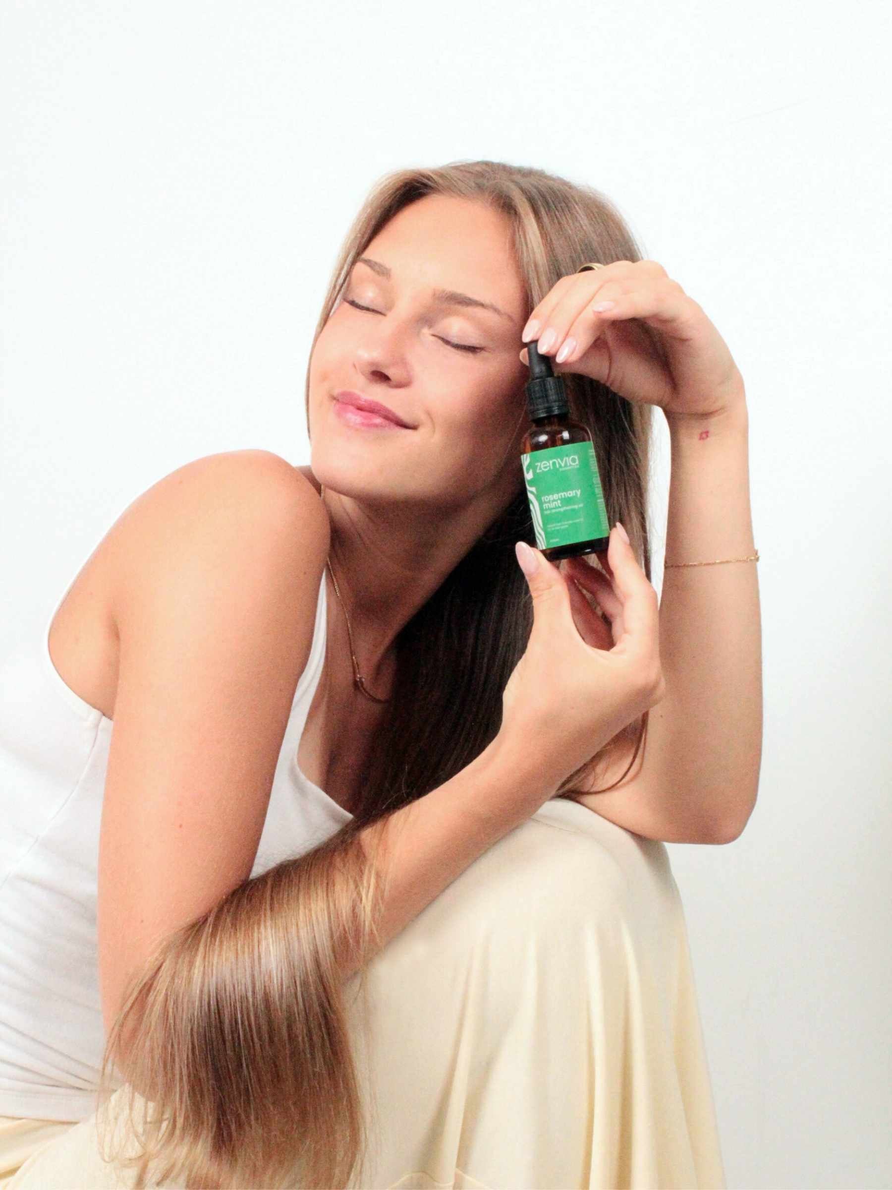 Woman holding a bottle Zenvia Rosemary Oil against a white background